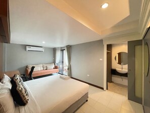 A modern hotel room with a large bed, a sofa, a bathroom with a mirror and sink, and an air conditioning unit. - Hub53 Coworking & Coliving Space (Chiang Mai)