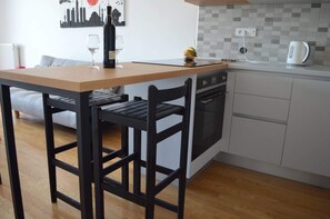 Een kleine keuken met een houten tafel, zwarte stoelen, een witte oven en een betegelde achterwand.