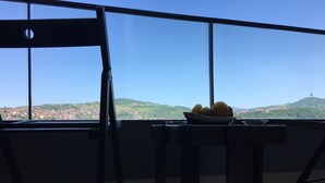 Un balcon avec une table et une chaise, donnant sur un paysage urbain avec des collines et une tour.