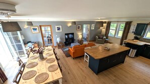 Un vaste espace de vie comprenant un coin repas avec une table en bois, un canapé orange et une cuisine dotée d’un grand îlot central.