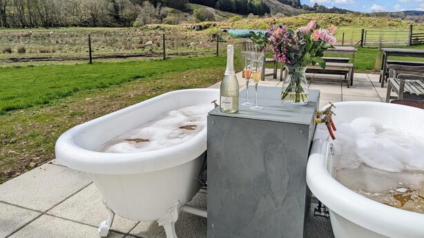 Deux baignoires blanches sur une terrasse, offrant une vue pittoresque sur un champ verdoyant et des collines.