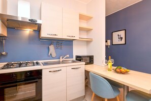A modern kitchen with white cabinets, a gas stove, and a microwave. There is a sink with a faucet, and a blue chair at the dining table. - Desenzanoloft Le Château de Margot  (Desenzano del Garda)