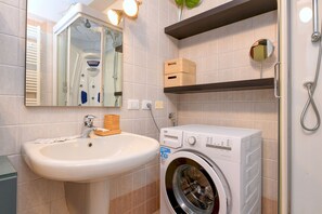 A bathroom with a sink, a washing machine, a mirror, and a shower. - Desenzanoloft Le Château de Margot  (Desenzano del Garda)