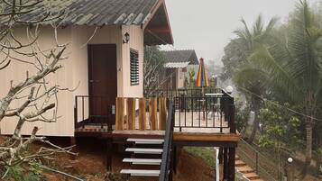 A house with a wooden deck, a staircase leading to a porch, and a view of a garden with palm trees.