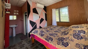 Ein Schlafzimmer mit Holzwand, einem Bett mit floralem Überwurf, einem Fenster mit Vorhängen und einer Decke mit dekorativen Verzierungen.
