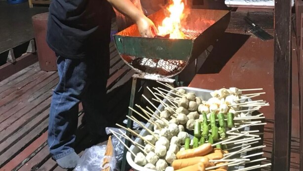Jemand grillt draußen, ein Feuer im Grill ist sichtbar.