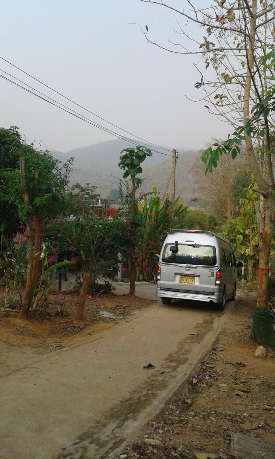 A silver van parked on a dirt road with vegetation on both sides.