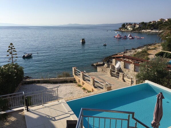 A swimming pool with a view of the sea, a stone building, and a beach area.