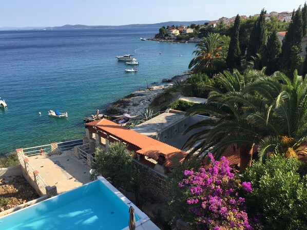 En fastighet vid kusten med en swimmingpool, utsikt över havet och en klippig strand med växtlighet.