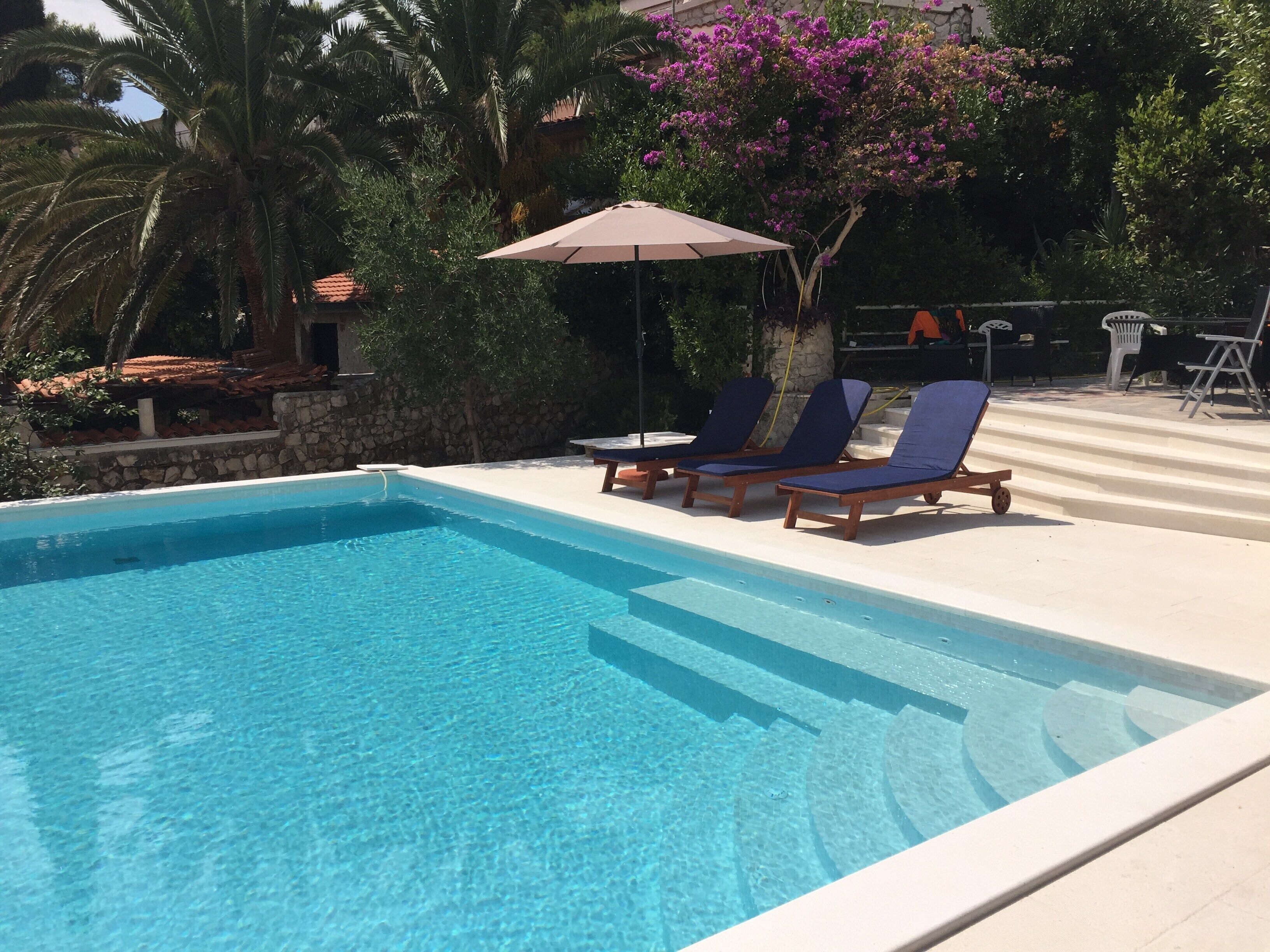 A clear blue swimming pool with lounge chairs and an umbrella.