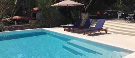 A clear blue swimming pool with lounge chairs and an umbrella.