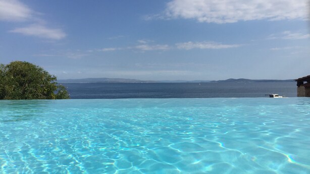 En klarblå pool med utsikt över havet och avlägsna berg.