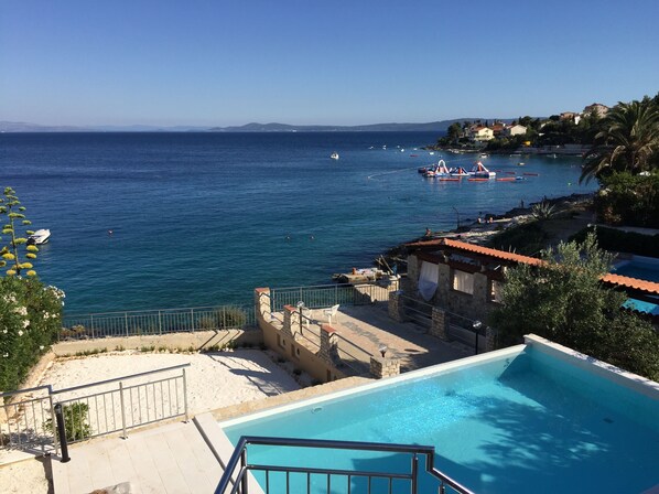 A coastal view with a swimming pool, a sandy beach, and boats on the water. - Beautiful villa with amazing swimming-pool, seafront (Okrug Gornji)