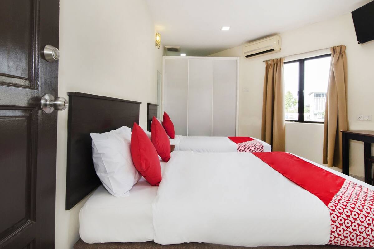 A hotel room with a bed, a wardrobe, a window with curtains, and an air conditioning unit.