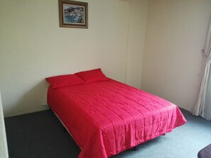 A single bed with a red bedspread in a room with a plain white wall and a framed picture above it. - MAJESTIC VIEW APARTMENT PANAJACHEL (Panajachel)