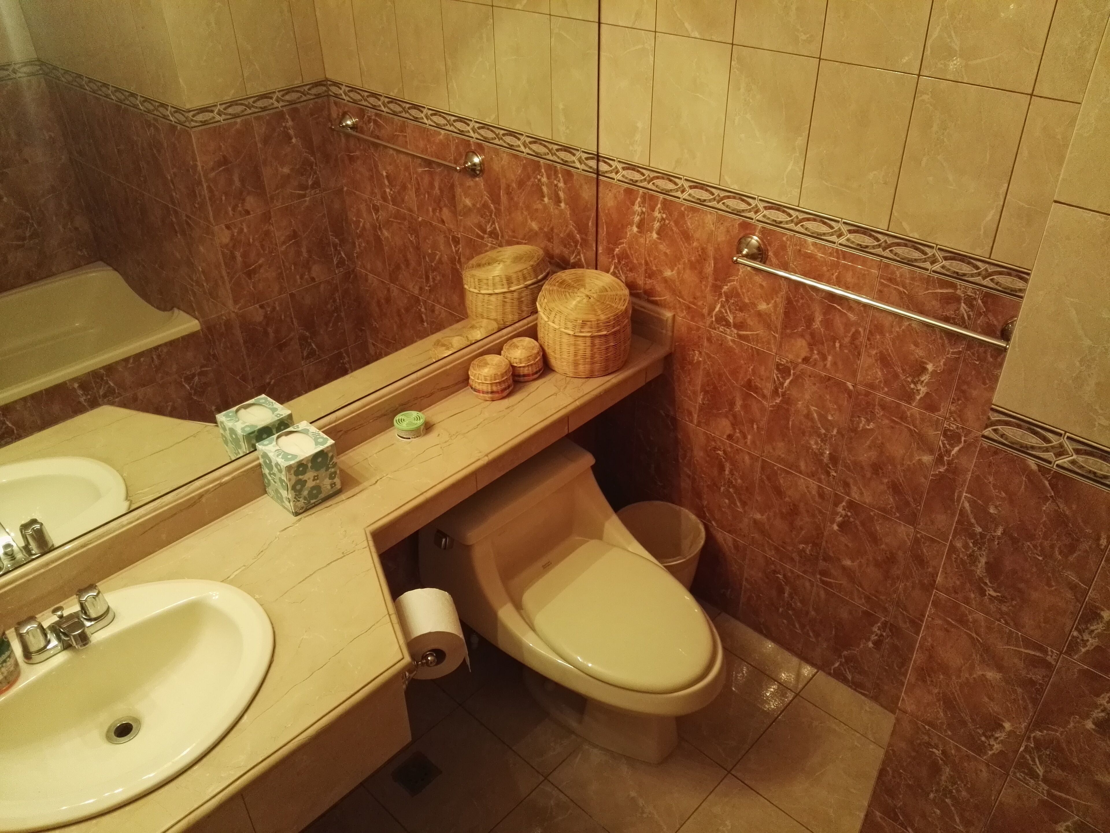 Ein Badezimmer mit Waschbecken, Toilette und Spiegel. Auf der Ablage liegen Körbe und an der Wand befindet sich ein Handtuchhalter.