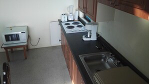 Une cuisine compacte équipée d’un four à micro-ondes, d’un grille-pain, d’un mixeur et d’une machine à café, le tout posé sur un plan de travail noir.