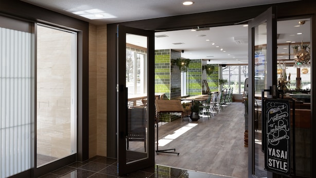 A modern interior with a glass door leading to a dining area, a sign reading "Welcome to YASAI STYLE," and a view of the outside through large windows. - Center Hotel Narita 2 R51 (Narita)