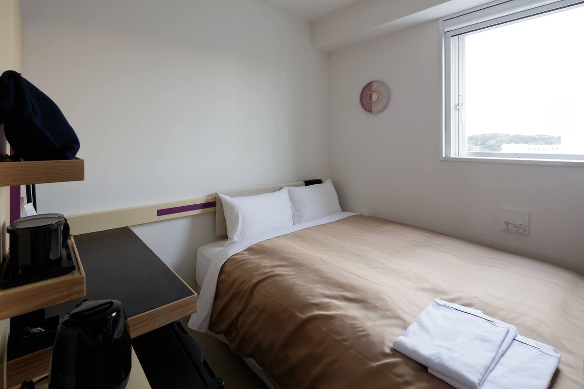 A hotel room with a bed, a desk with a coffee maker, and a window.