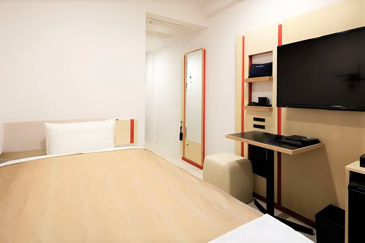 A hotel room with a bed, a desk, a chair, a TV, and a wardrobe.