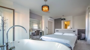 Een moderne hotelkamer met een groot, wit bad, een apart bureau en een comfortabel bed.