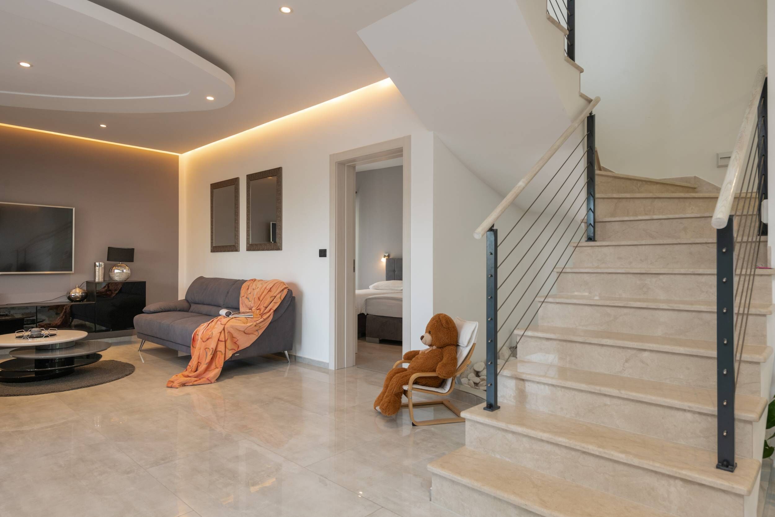Un salon moderne avec un canapé, un fauteuil, un ours et un escalier.