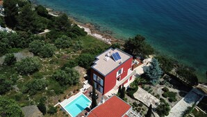 A modern two-story house with a swimming pool, surrounded by lush greenery and a rocky coastline. - Villa With Private Pool (Kukljica)