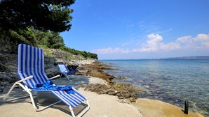 A beach with two striped lounge chairs and a rocky shoreline. - Villa With Private Pool (Kukljica)