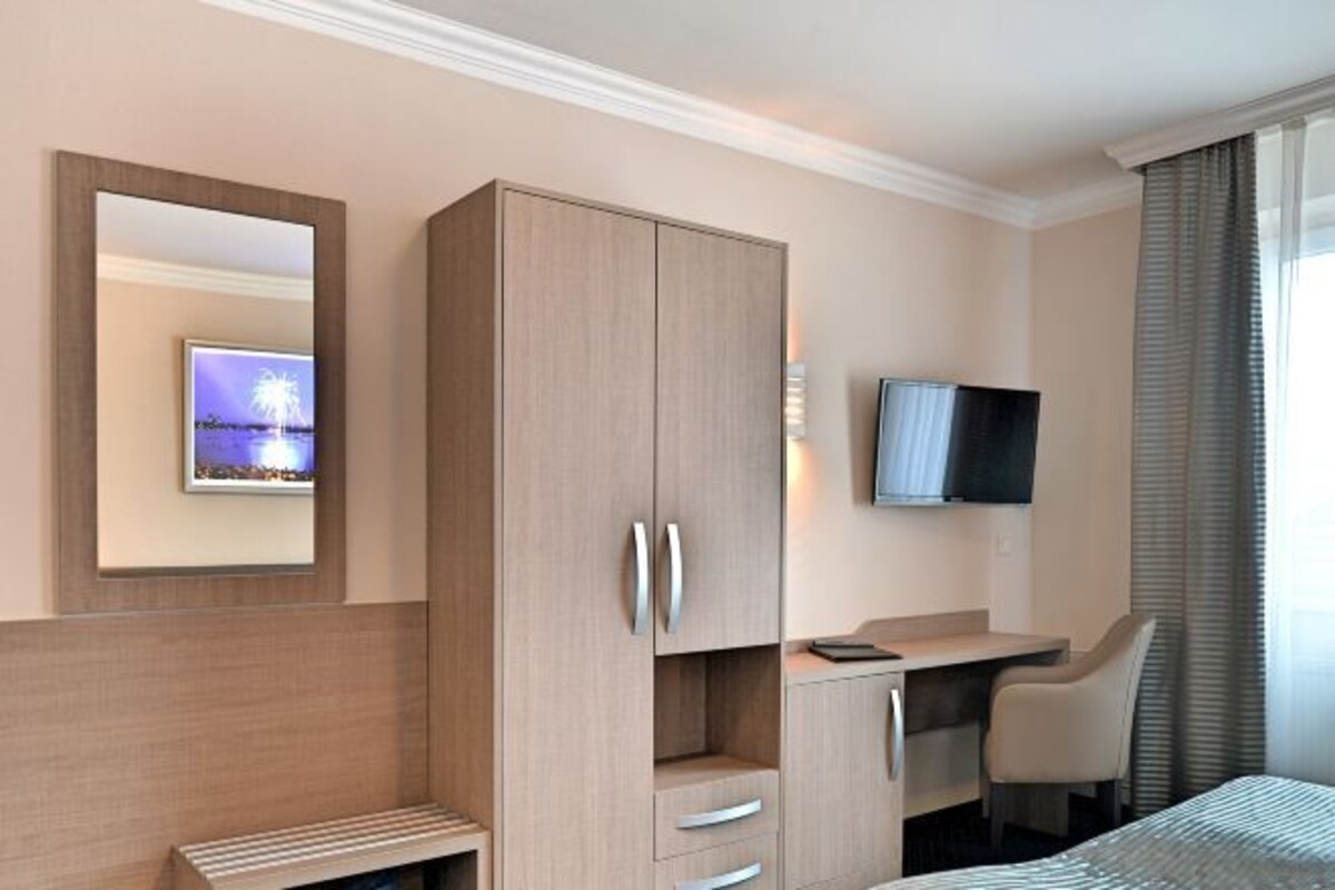 Een hotelkamer met een bed, een bureau met stoel, een kledingkast, een televisie en een spiegel.