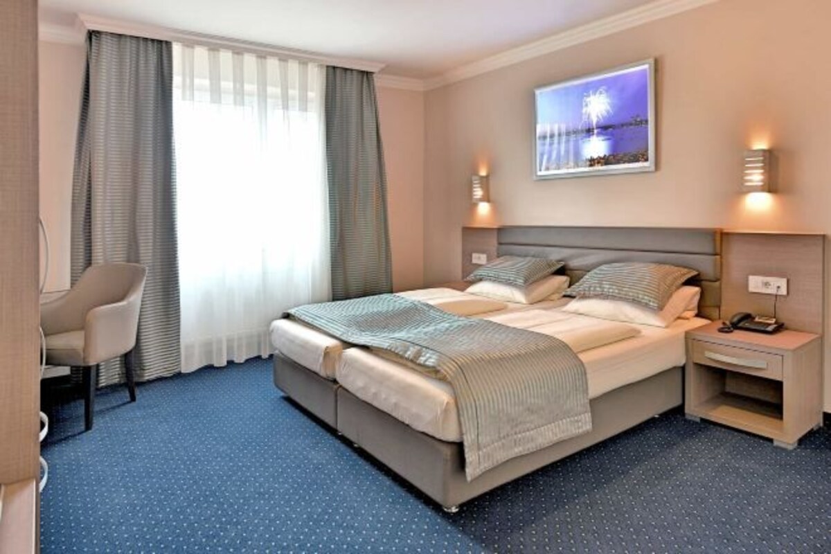 Een hotelkamer met een bed, nachtkastjes, een stoel en een groot raam met gordijnen.