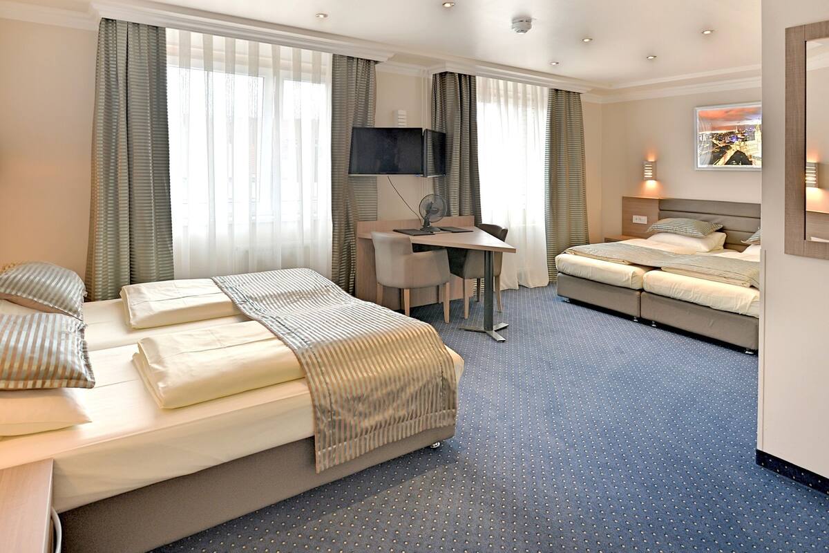 Ein Hotelzimmer mit einem großen Bett, einem Schreibtisch, einem Fernseher und einem weiteren Bett.