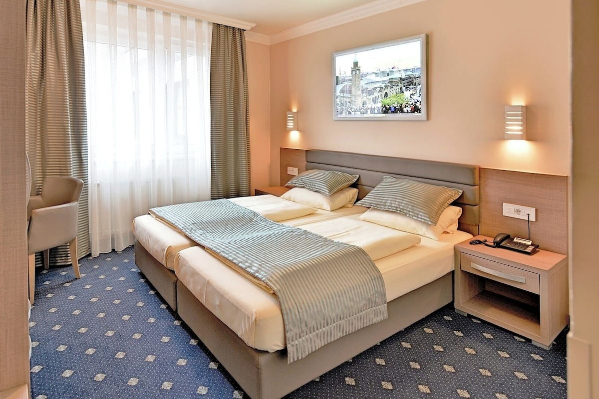 Ein Hotelzimmer mit einem großen Bett, einem Schreibtisch, einem Stuhl und einem fenster mit Vorhängen.
