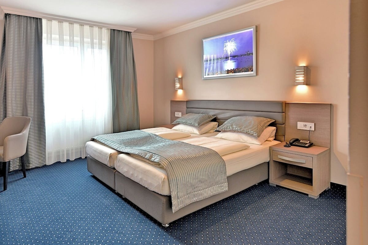 Ein Hotelzimmer mit einem großen Bett, einem Schreibtisch, einem Sessel und einem Fenster mit Vorhängen.