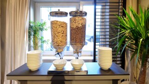 Ein Frühstücksbuffet mit zwei großen Behältern für Granola und Schüsseln mit Müsli auf einem Tisch.