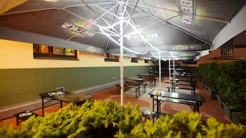 Un comedor interior con mesas y bancos, un techo con una lámpara de diseño geométrico y una pared con una vista parcial de una ventana.