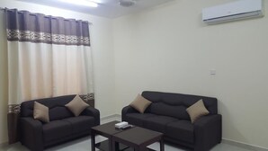 A living room with two dark sofas, a coffee table, and a window with curtains. - Today House Suites (Salalah)