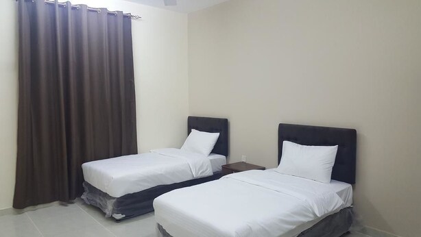 A hotel room with two single beds, a nightstand, and a curtain. - Today House Suites (Salalah)