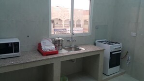 A small kitchen with a microwave, sink, and gas stove. - Today House Suites (Salalah)