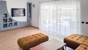 A modern living room with a flat-screen TV, two brown sofas, a wooden coffee table, and a large window with sheer curtains. - Cozy home in Galizana (Galizana)