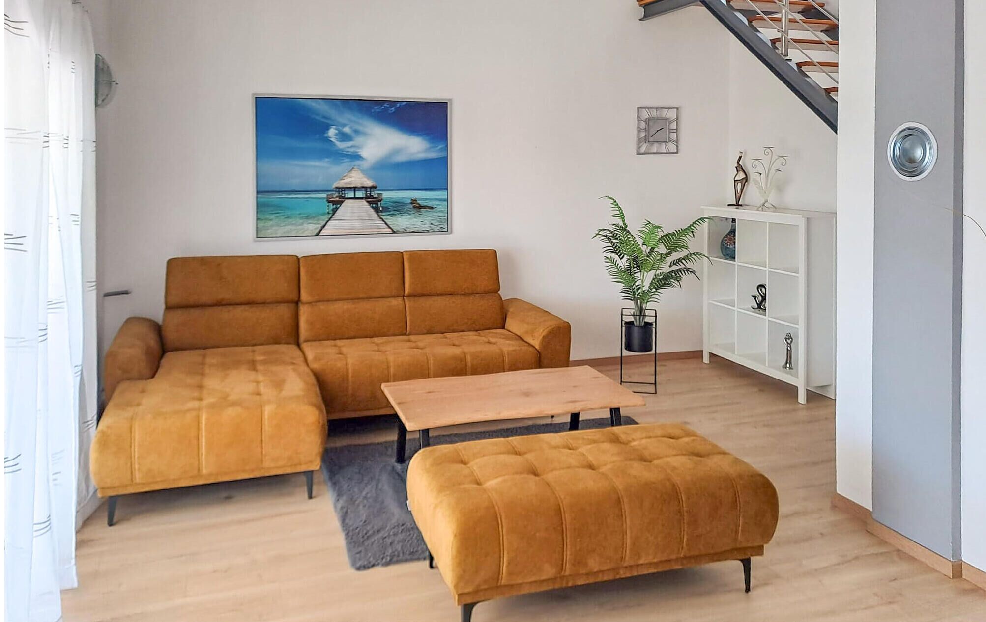 A living room with a sofa, ottoman, and a painting of a beach scene.