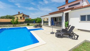 A swimming pool with lounge chairs and umbrellas, a white building with a tiled roof, and a stone wall in the background. - Cozy home in Galizana (Galizana)