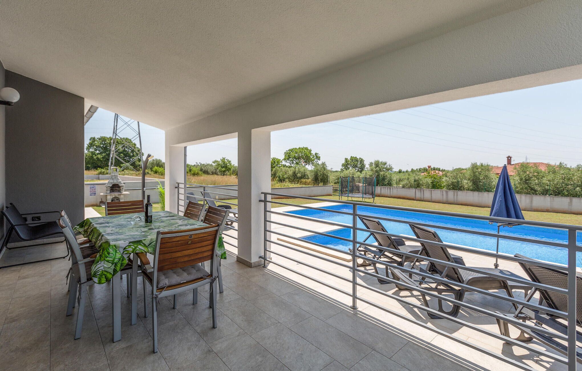A covered outdoor area with a pool, seating, and a barbecue grill.