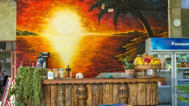 A wooden counter with a mural of a sunset and palm trees, a Panasonic refrigerator, and various items on the counter. - Pai Backpackers Paradise - Adults Only (Pai)
