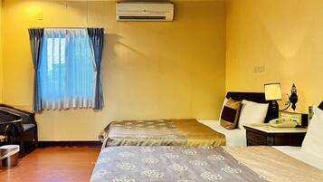 A hotel room with two beds, a desk, a chair, a telephone, and an air conditioning unit.
