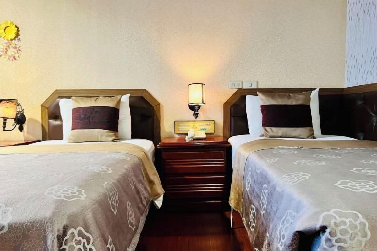 Une chambre d’hôtel avec deux lits, une table de chevet avec une lampe et un luminaire fixé au mur.