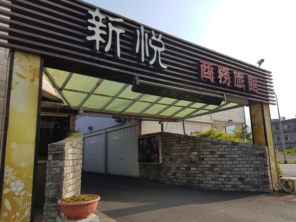 Entrada de hotel con un letrero que dice “新悦 商旅馆” y un área de recepción techada.