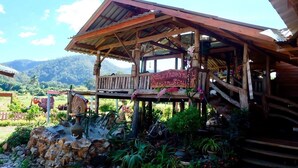 A rustic wooden structure with a balcony, surrounded by potted plants and a stone wall. - Wongwan Farm (Samoeng)