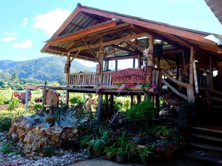 A rustic wooden structure with a balcony, surrounded by potted plants and a stone wall.