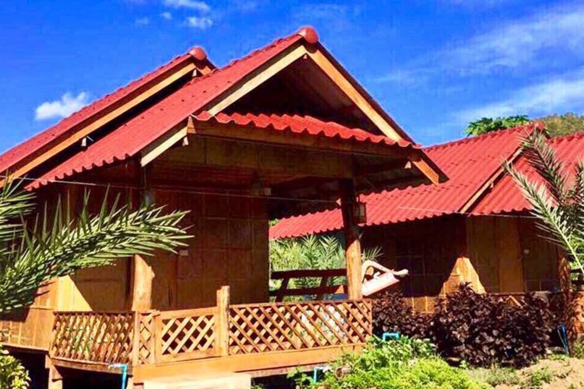 Una casa de madera con techo rojo, rodeada de follaje y un cielo despejado.
