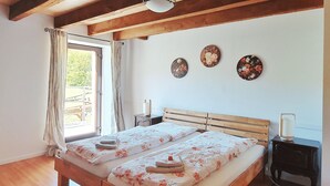 A double bed with floral bedding, wooden headboard, bedside tables with lamps, and a view of a deck through a window with curtains. - renovated farmhouse for groups and families in nature, dogs welcome, playground (La Chapelle-devant-Bruyères)